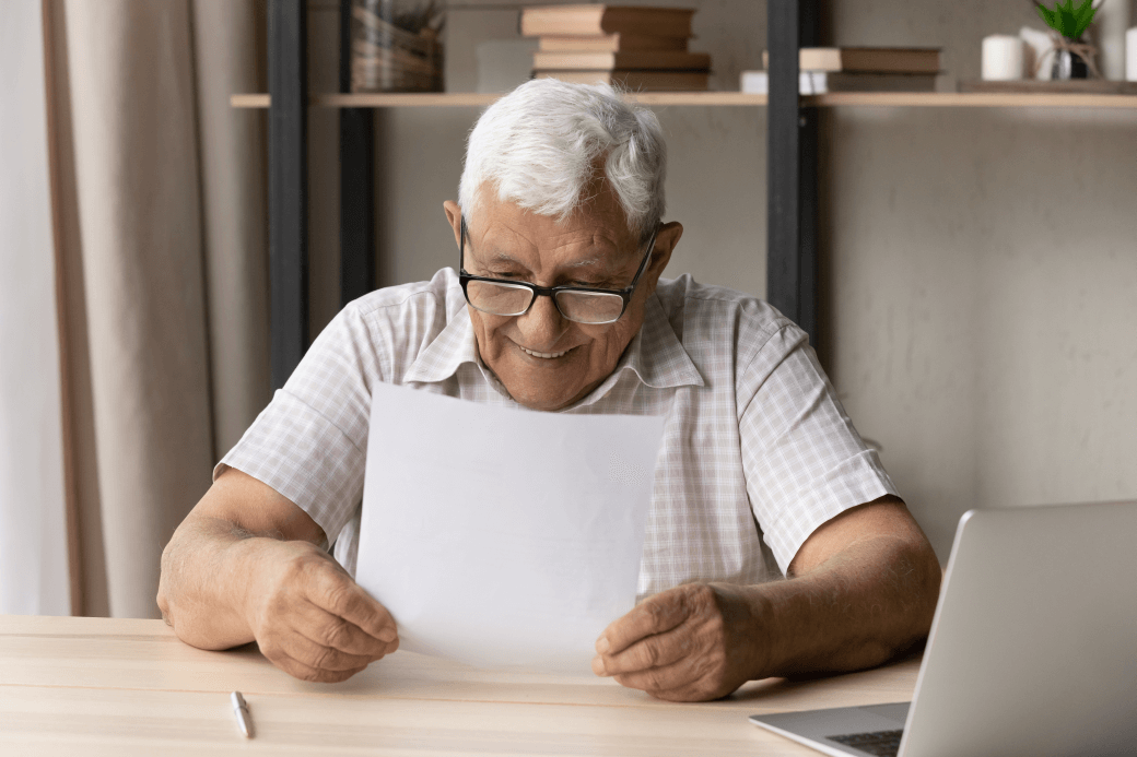 elderly man reading a document about upcoming changes to aged care services and legislation: he is smiling as he reads knowing that he has planned for the changes with his professional adviser; he is comfortable that his investment success has rewarded his patience