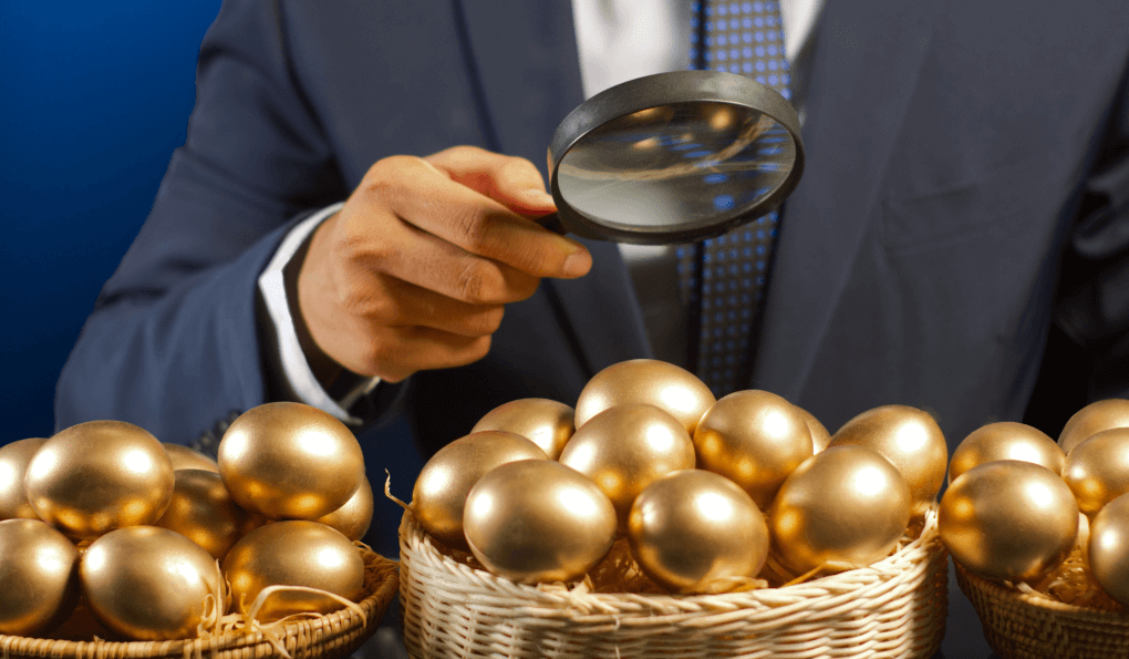 a suited male uses a magnifying glass as he inspects three nest egg baskets of golden eggs seeking awareness of superannuation investment outcome comparisons