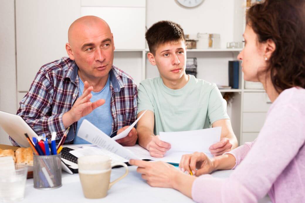 mother, father and young son gathered at the kitchen table to review and strategise the investment for income for their child: with laptop and documents open, they review tax consequence of different holding structure options