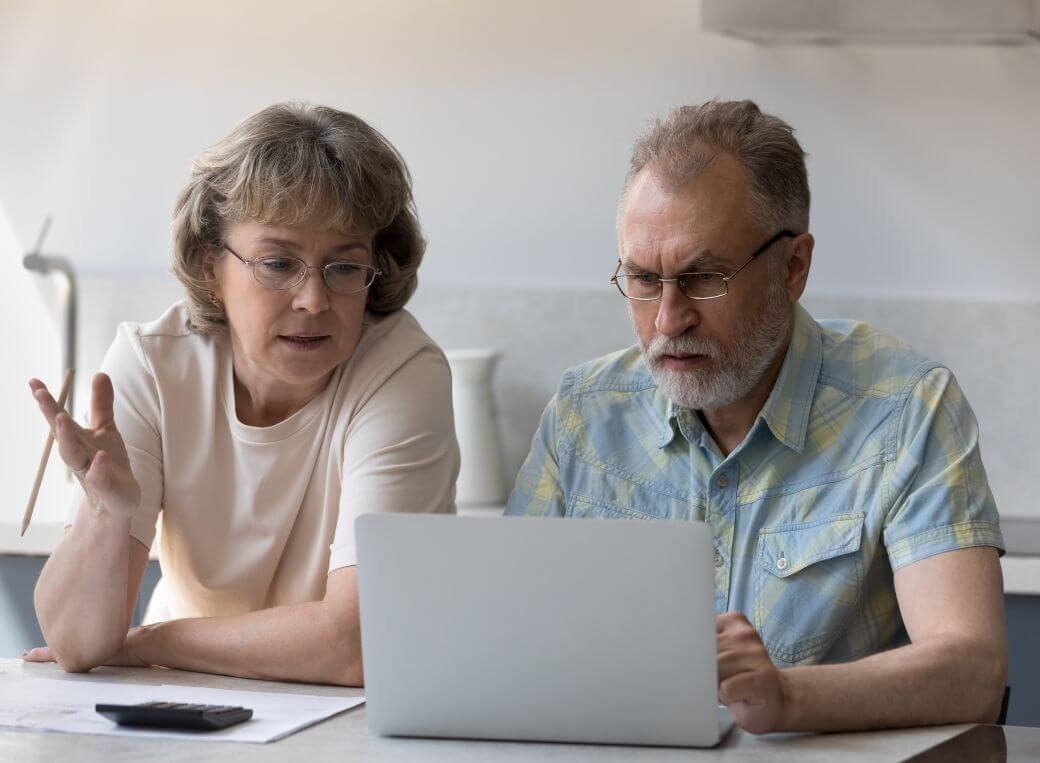 middle-aged couple reviewing the superannuation processes as they consider retirement and strategies including access to their super under relevant conditions of release - sitting at a home table, with laptop open calculator and work papers open
