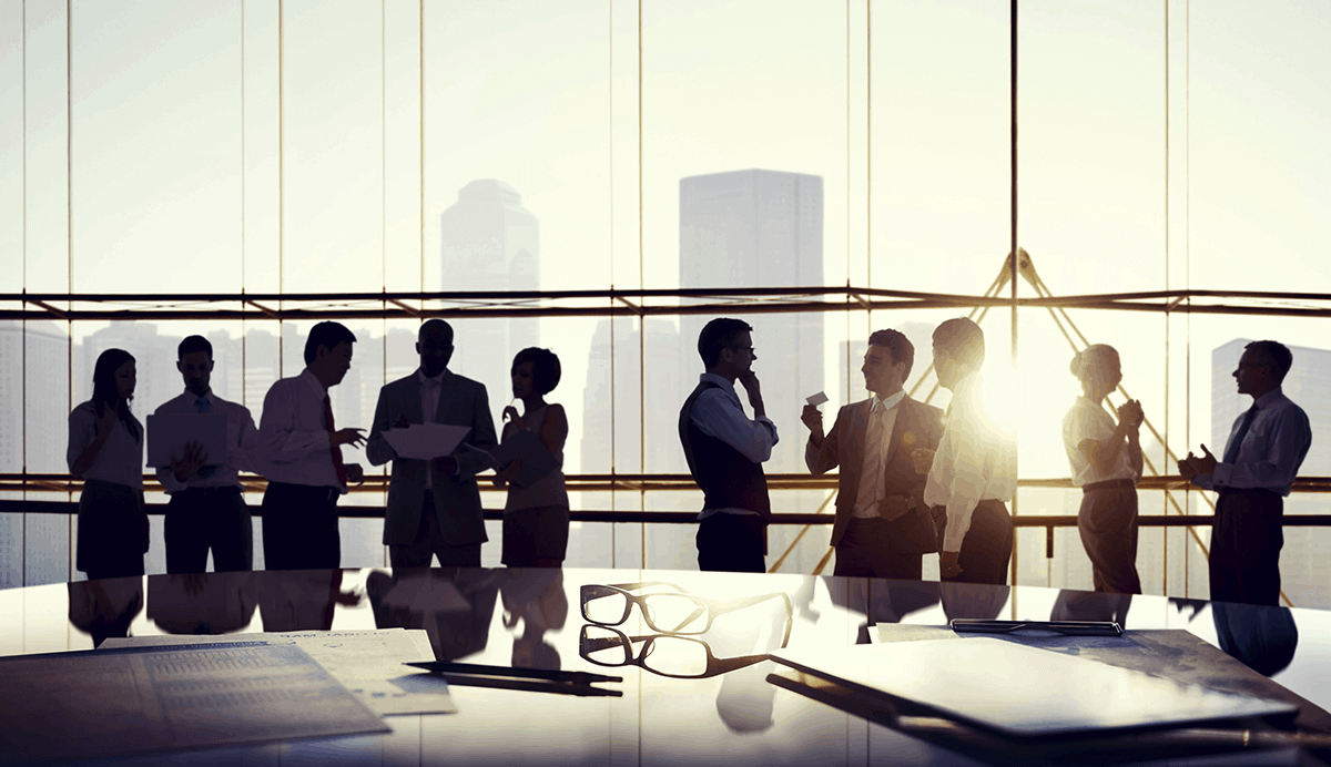 group of young professional people standing during a break in their meeting - views from the adjacent windows show them to be high in a building looking toward a city rooftop scape - discussing occupation definitions