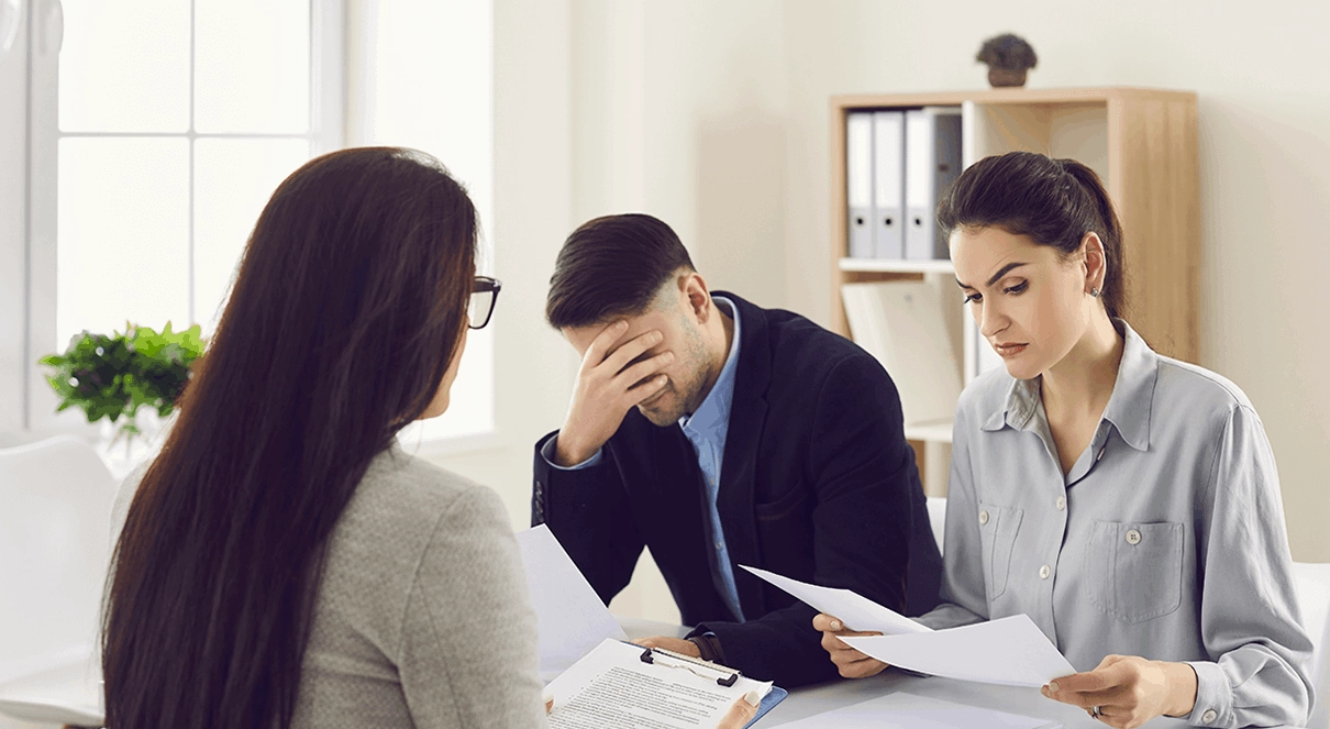 young couple being made aware of the shortcomings in the administration of their SMSF Trustee roles, by their adviser: the woman carefully taking it in whilst her male partner holds his head in despair