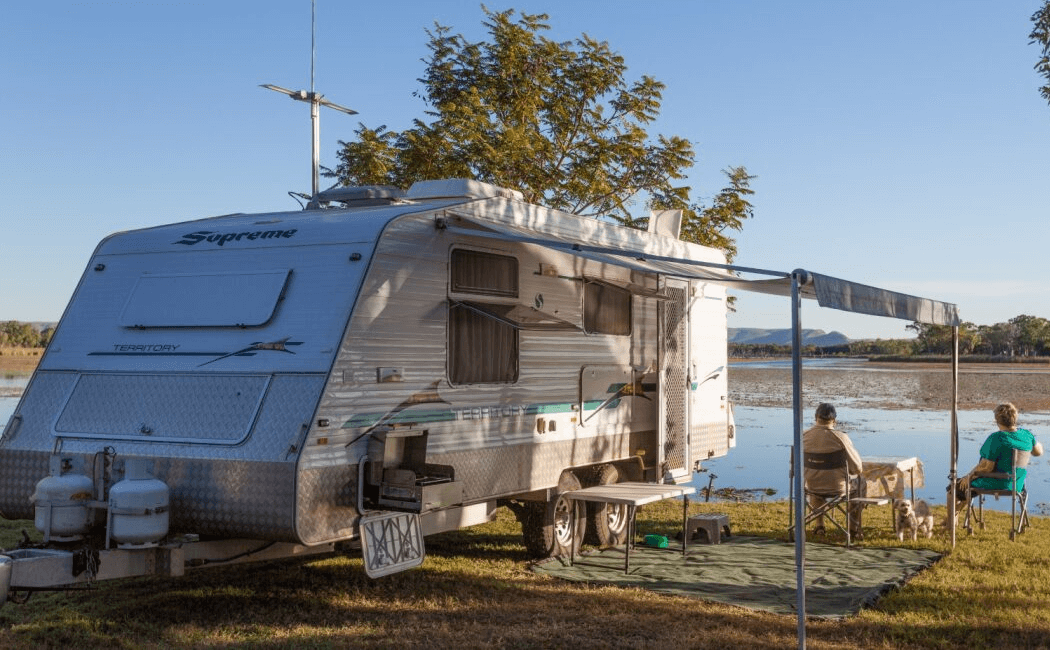 retired couple sitting alongside their caravan which they have parked at a river bank - depicting what their accumulated super has facilitated - saving in super in your 60s