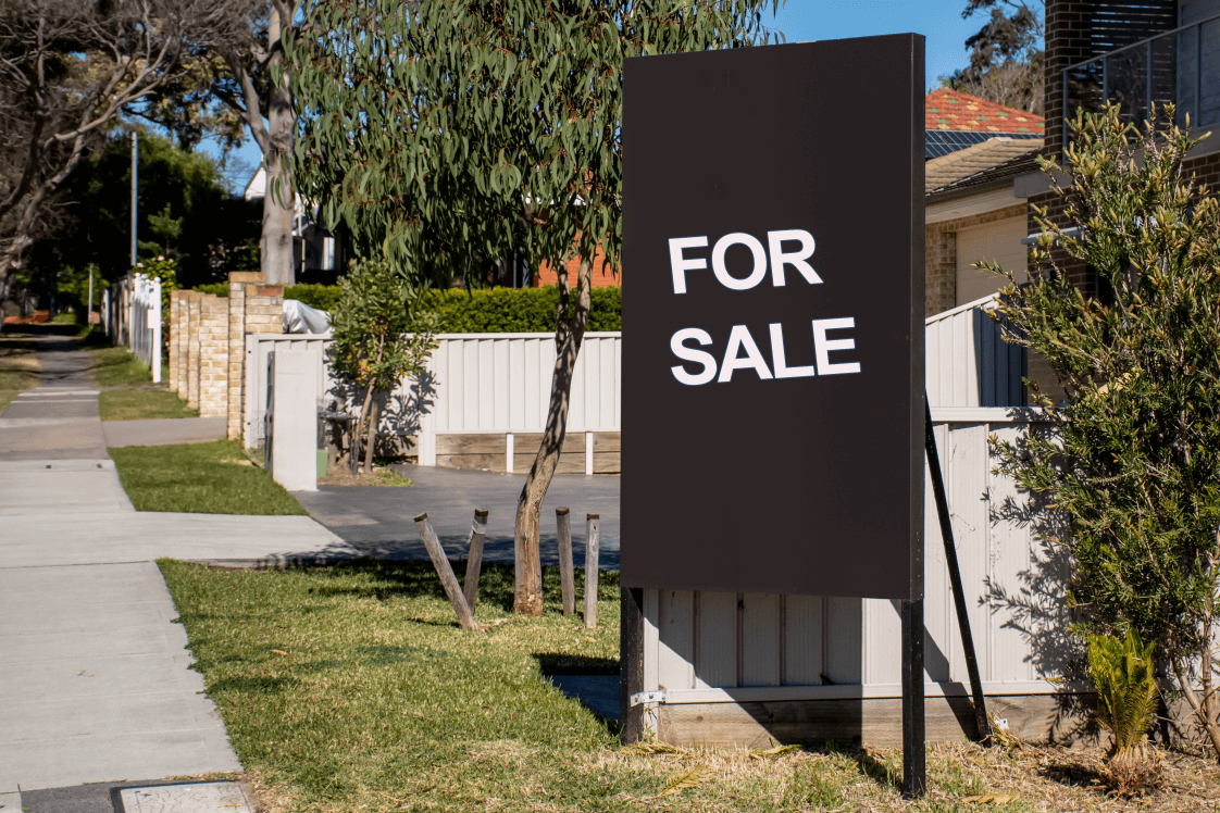 image of a prominent For Sale sign in a suburban street: sign is in white block lettering on a black background - depicting the myth that moving into residential aged care default requires selling your home whilst also highlighting the interest Australians have in property inverstment