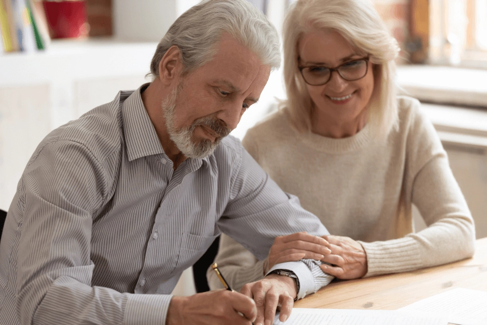 older couple with woman holding her male partners arm as they signs documentation