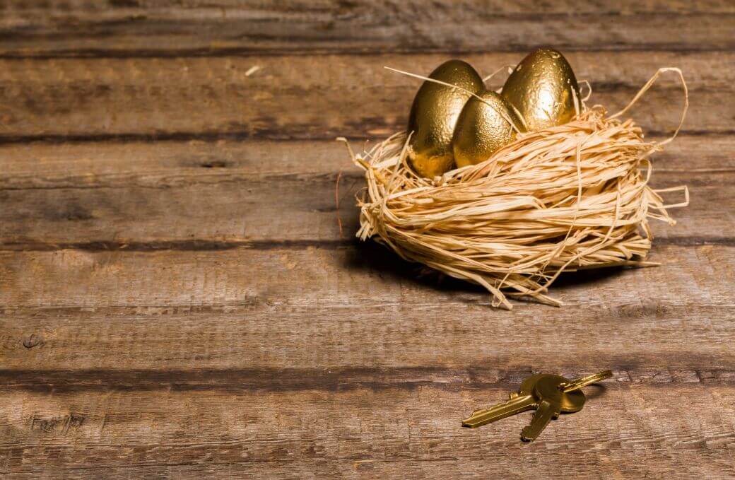 a woven straw nest containing three gold coated eggs sit on a rustic timber benchtop with a set of keys alongside the nest - symbolising superannuation nest-egg security; annuities as an underpin for retirement income