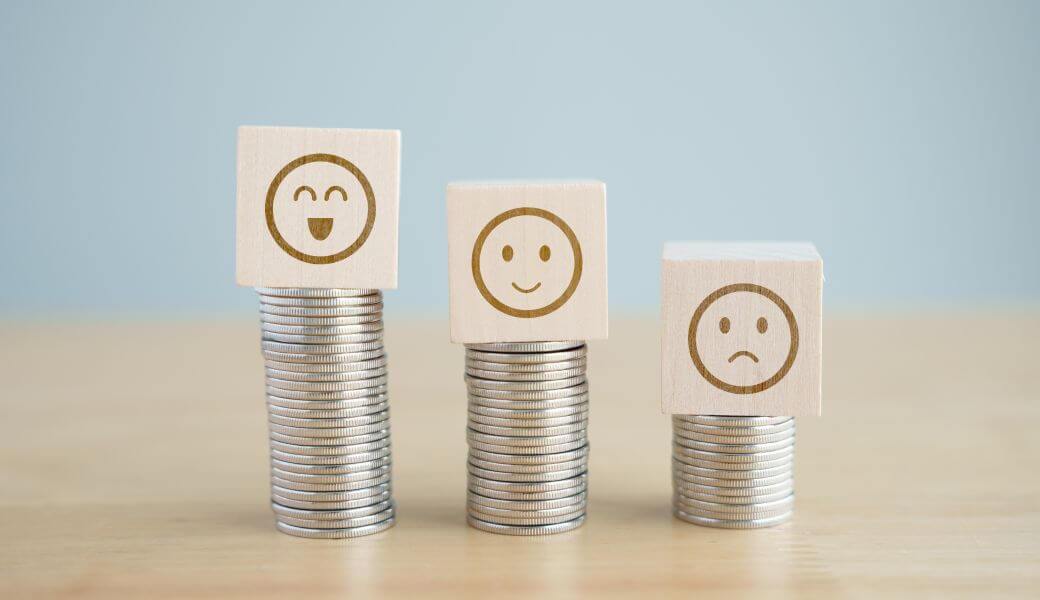 three stacks of coins of different heights; each is topped by a wooden block with an image of a 'circle' face. The one on the tallest stack is laughing, the mid-sized stack has a smiley face, and the small stack has a frown. These represent what is left of the different categories of termination payment after the tax has been deducted
