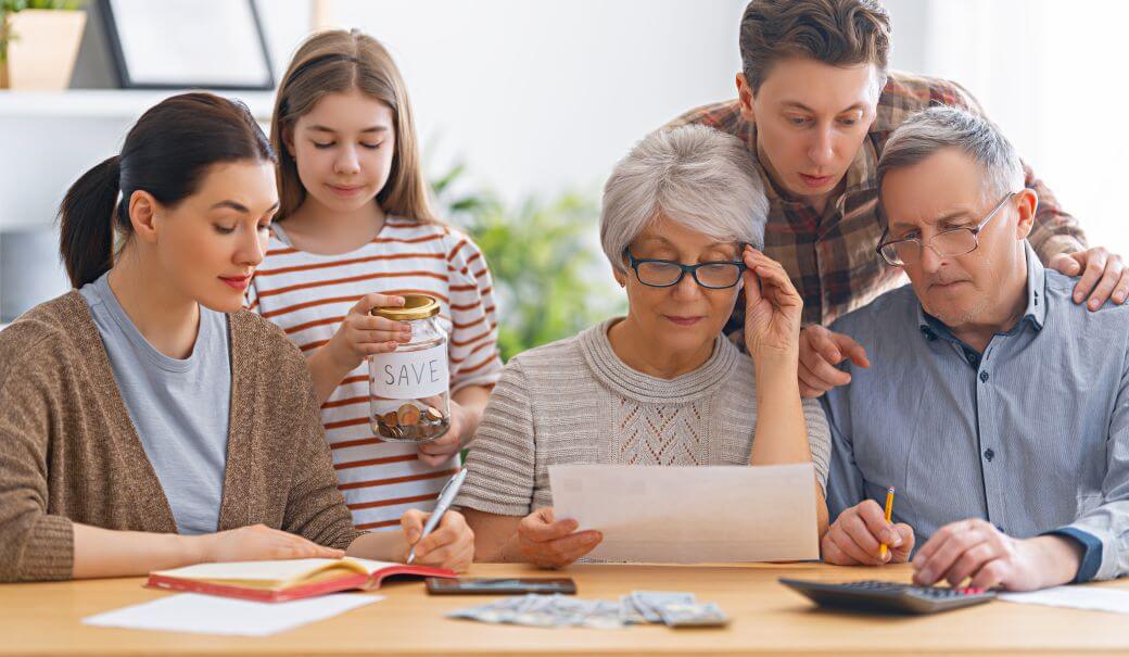 Grandparents and parents meet to consider arrangements to meet the rising cost of education for their child, standing in the background
