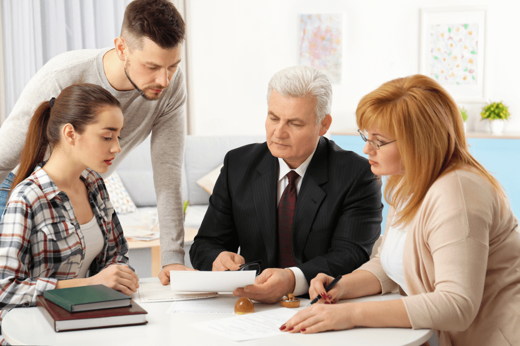 financial adviser explains the features and benefits of wealth management to three siblings seated around him at a table - application of testamentary trusts in to estate planning