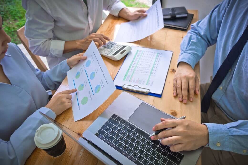 Investment advice team working together on a strategic investment asset class allocation with appropriate diversification for a client: they are reviewing a laptop and printed reports