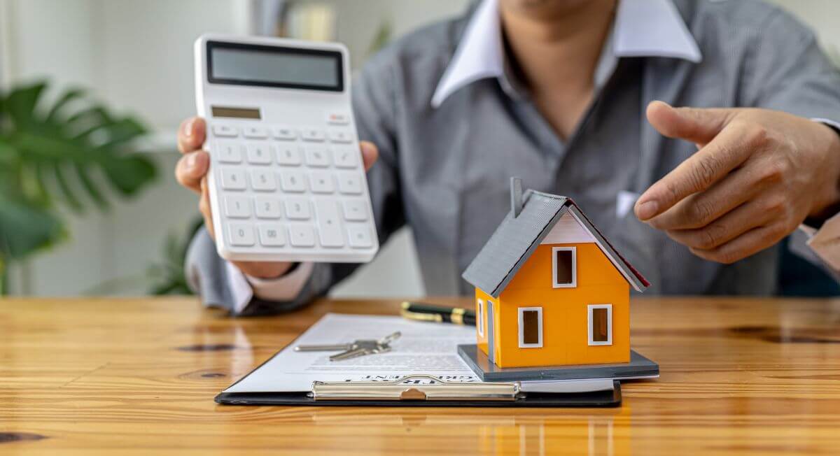 adviser shows a calculator and a miniature model of a house to his client as the financial consequences of selling or retaining the family home to finance entry to residential aged care are contemplated