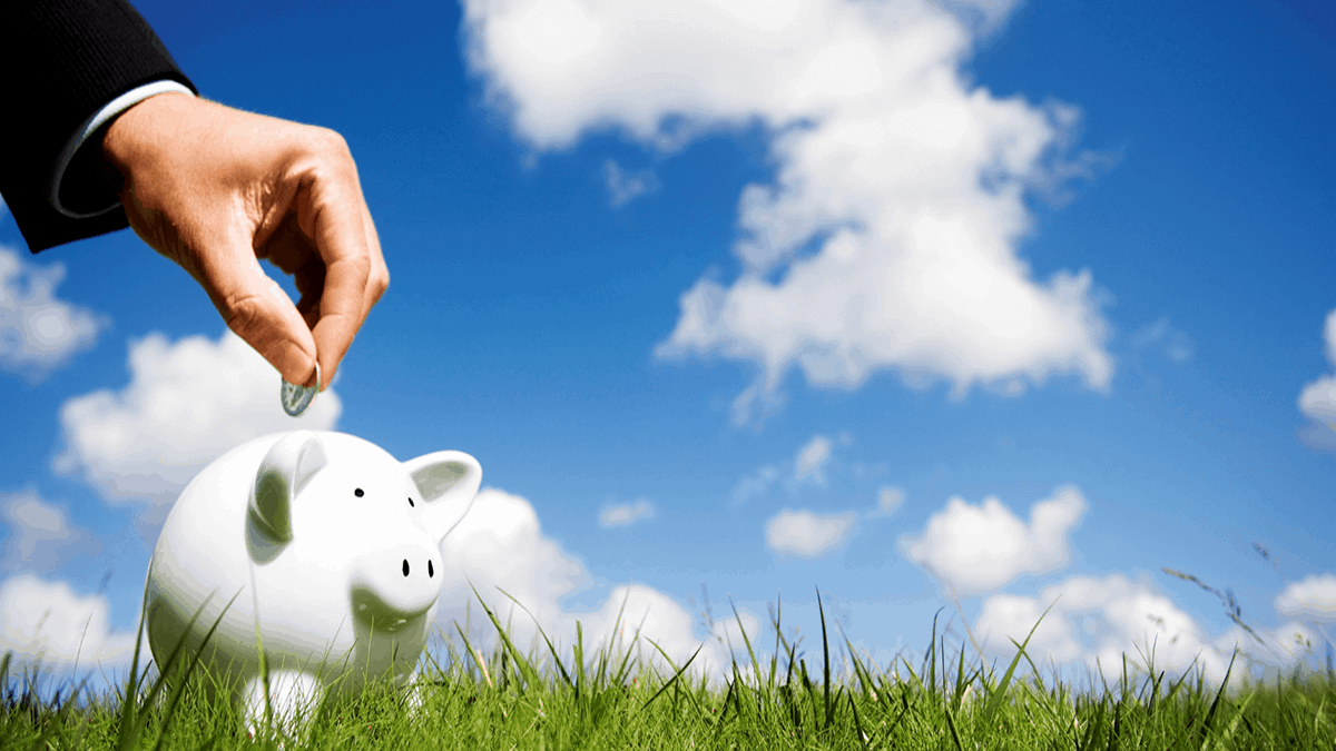 white piggy bank on a green grass lawn under a lightly clouded sky and with a man making a monetary contribution into the piggy bank representing an eligible contribution to super; a prsonal superannuation account; or perhaps otherwise investing surplus cash