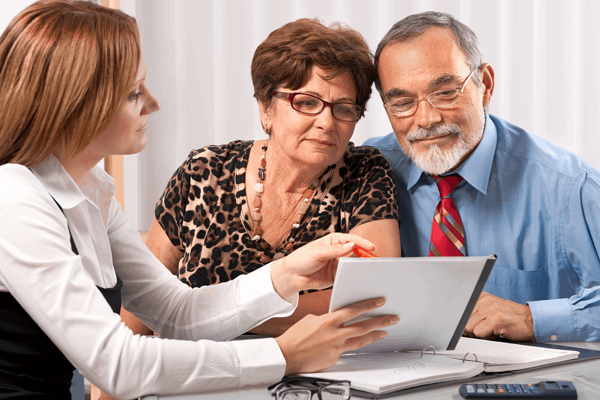 middle aged couple examine a document presented to them by their financial planner - a female, as they contemplate their recommendation for a self-funded income stream