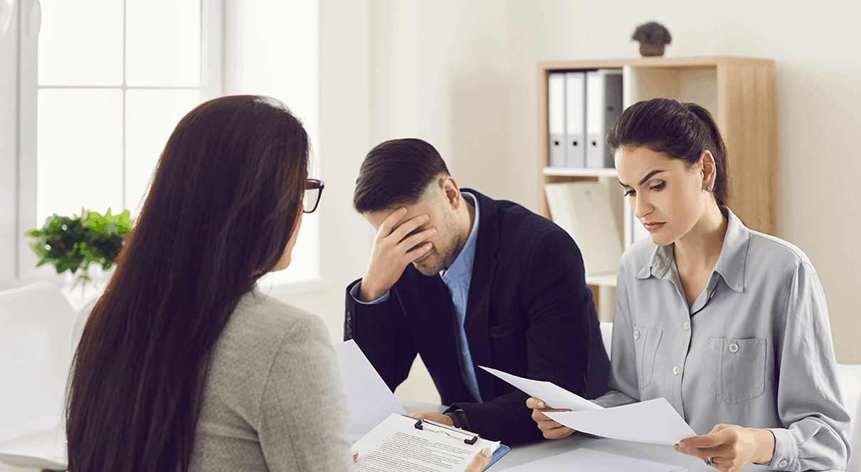 young couple being made aware of the shortcomings in the administration of their SMSF Trustee roles, by their adviser: the woman carefully taking it in whilst her male partner holds his head in despair