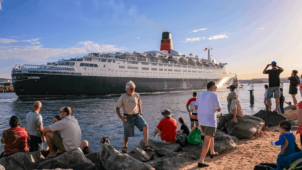 image of a passenger liner ship docking to collect a new group of passengers, being watched over by some people seeing this travel as part of their retirement dreams