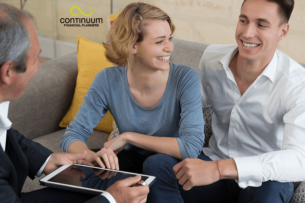 youngish couple sitting opposite their financial planner receiving a report on their investment strategy review: their smiles suggest their satisfaction with the review report