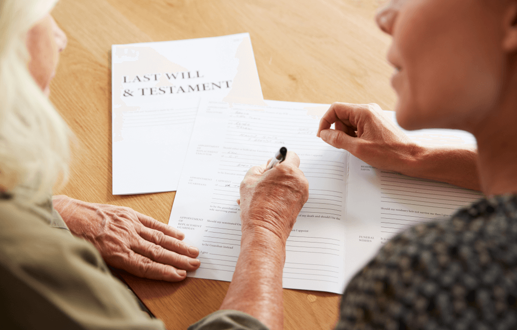 older lady signing her last will and testament being guided by a younger lady friend - estate planning foundation is a valid will