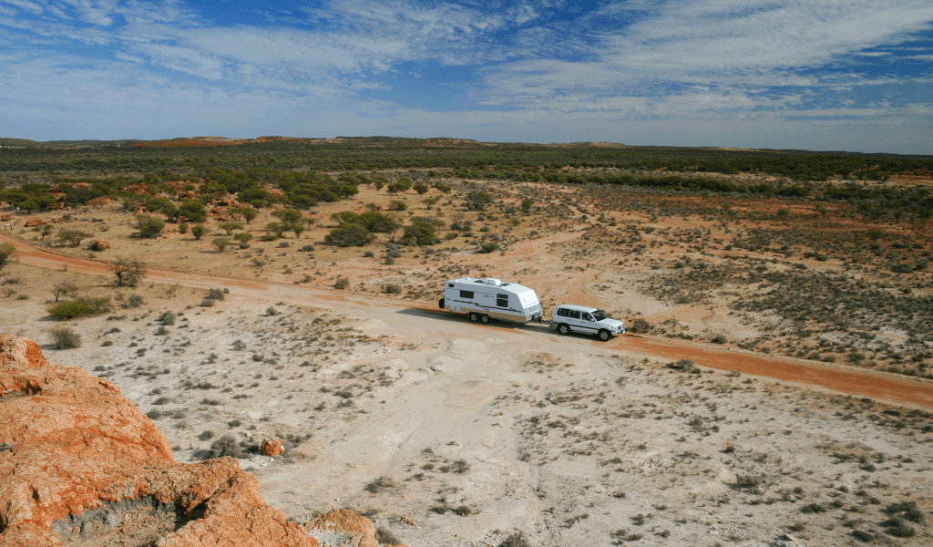 a 4WD vehicle towing a large caravan across an outback track through sparsely vegetated dry region - having made timely arrangements for funding early retirement