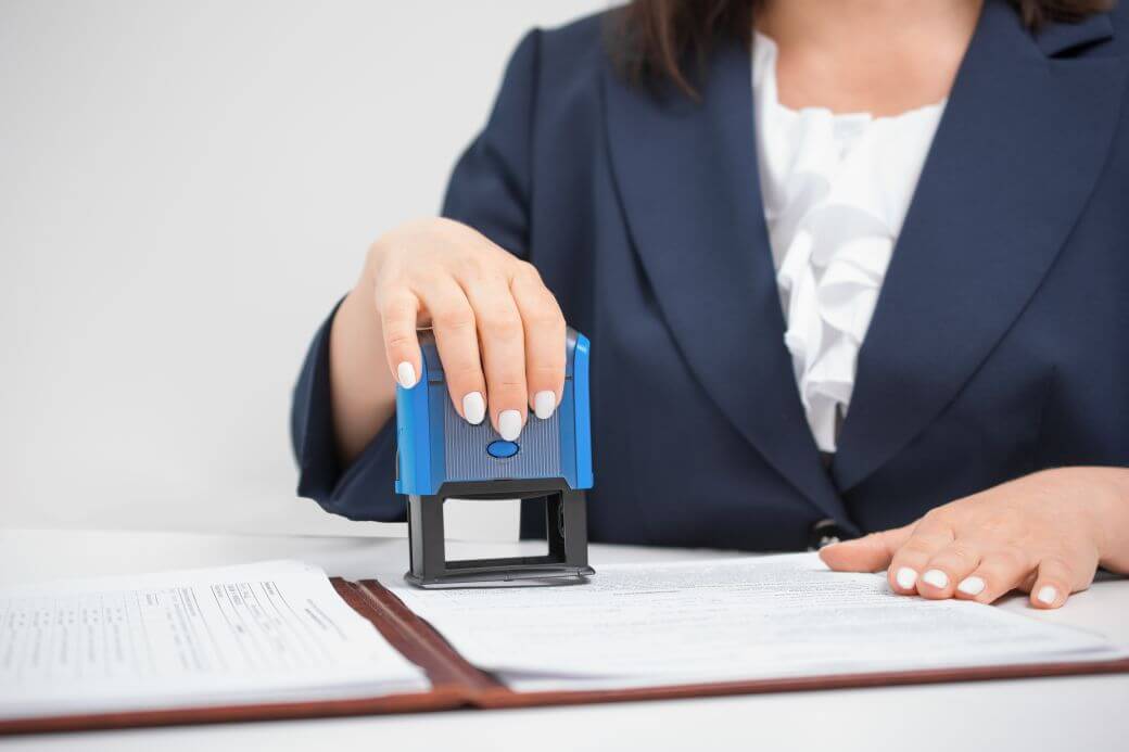 female clerk in a blue jacket and a white blouse applying a stamp approving an application for an Investment Bond used in an Estate Planning Case Study