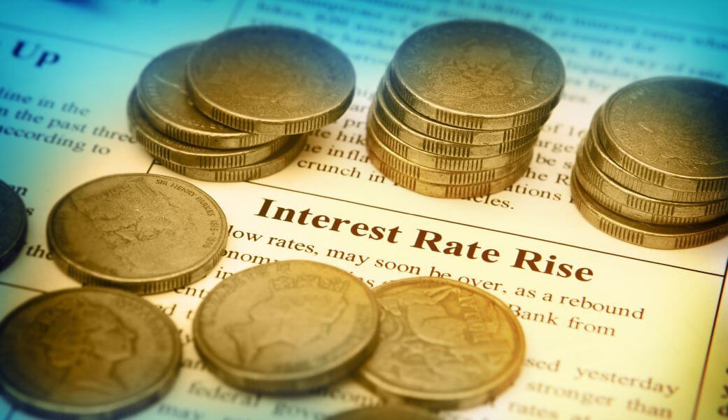small piles of AUD1 coins and some scattered loose on an artcile in a magazine showing that low interest rates are ending, interest rates rise