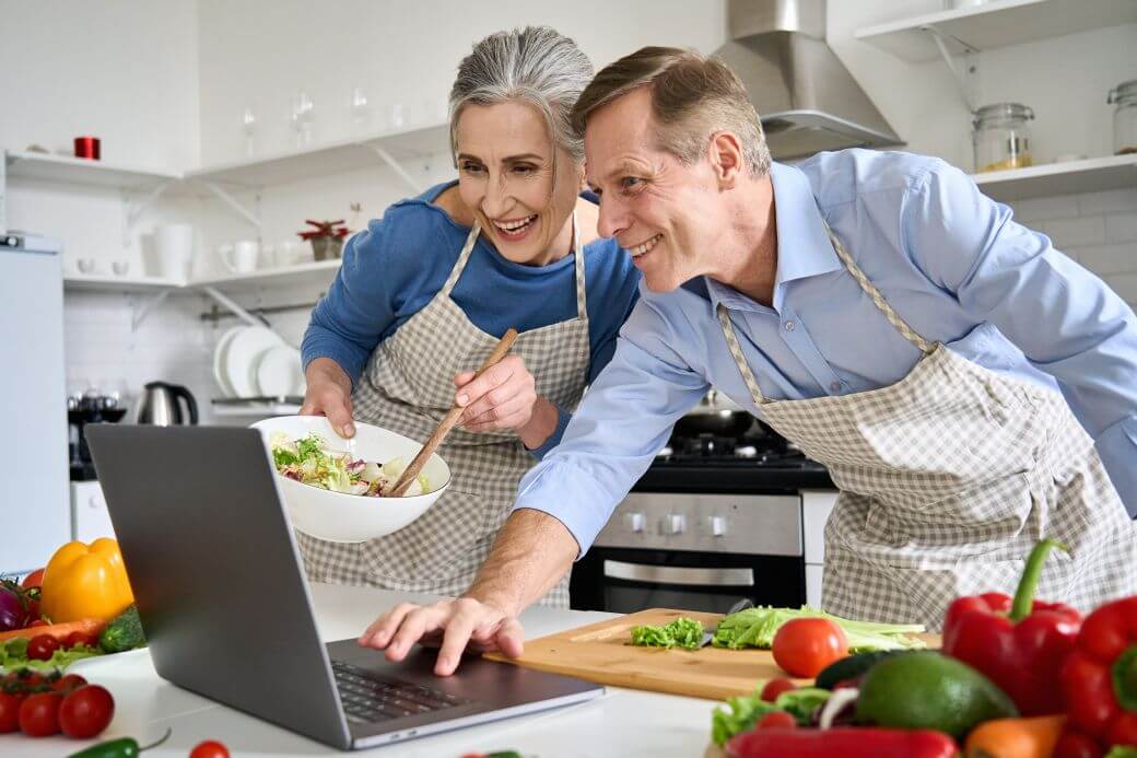 happy and relaxed middle-aged couple working together in the kitchen practising skills and pastimes they will participate in as they transition to retirement