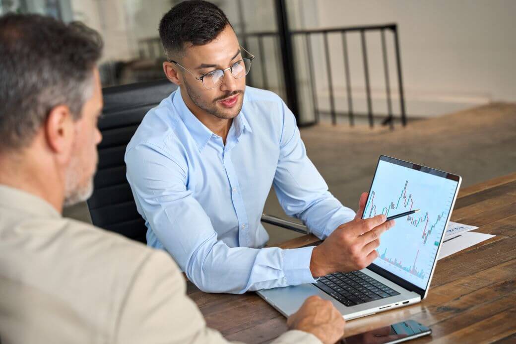 an investor meets with his financial adviser and reviews on a laptop, the volatility of markets as reflected in a line chart - the general, long-term trendline is upwards