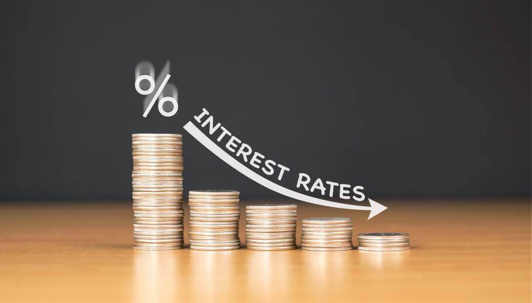 image of piles of coins sitting on a benchtop, decreasing in size from left to right. image is overwritten with a percentage sign. a downswooping arrow with the words interest rates following the arrow - an indication that interest rates are going to be lower for longer