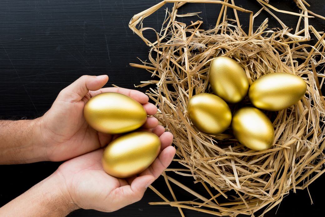 a nest egg of retirement funds building in superannuation - a man's hands adding more eggs suggesting he is managing his super wisely