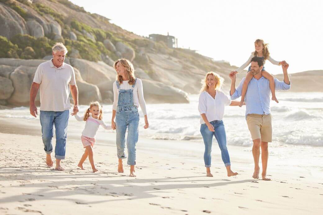 three generations of a family stroll happily on a beach, the elder comfortable with his superannuation and age pension strategy funding his retirement