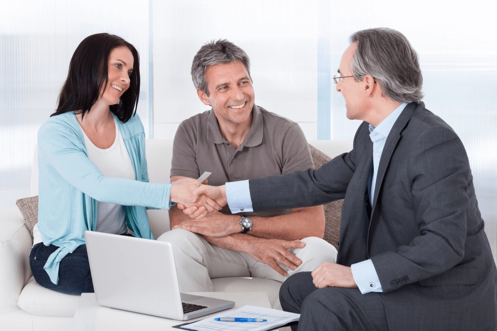 a casually dressed mid-aged couple receiving financial advice from their older adviser; the woman of the couple is shaking the hand of the adviser - confirming that financial advice matters