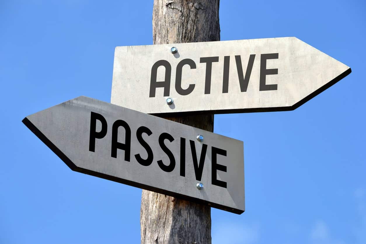 A signpost with two signs painted white and worded Active and Passive respectively in black lettering, attached to a wooden post, pointing in different directions, reflecting investment styles known by those names