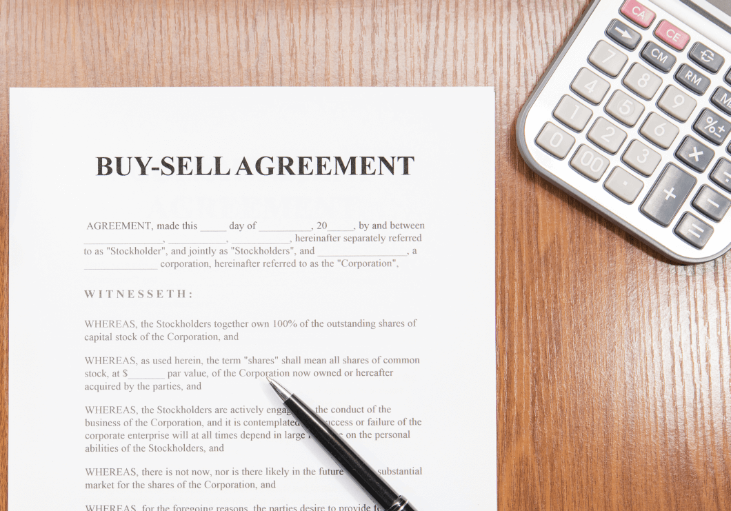 A Buy-Sell Agreement document on a desk alongside a calculator pending resolution of terms, conditions and valuation to formulate agreements
