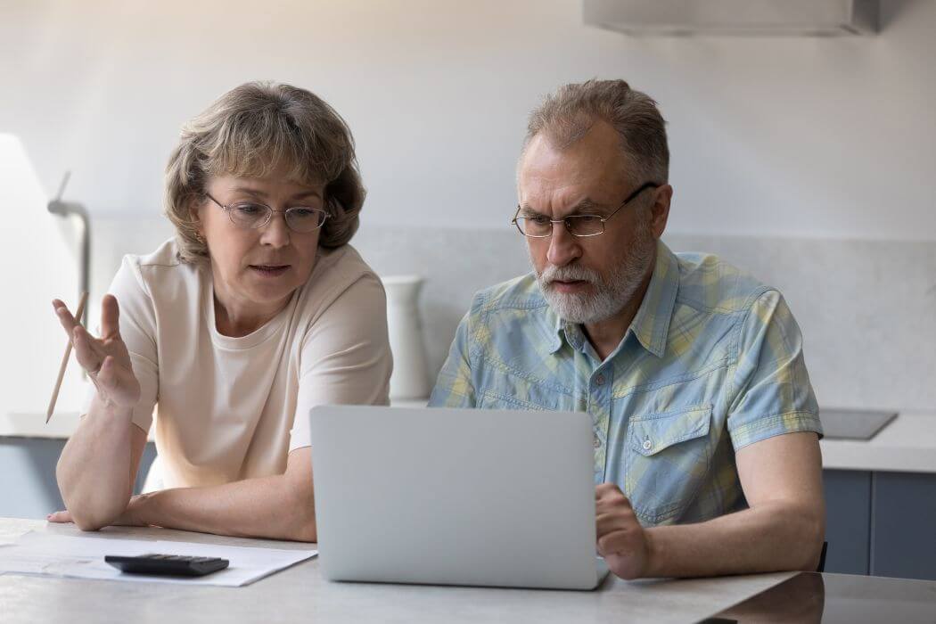 mid-aged couple pondering their future retirement as they peruse the numbers on the screen of the laptop open in front of them wanting to answer the question: how much can we spend in retirement?
