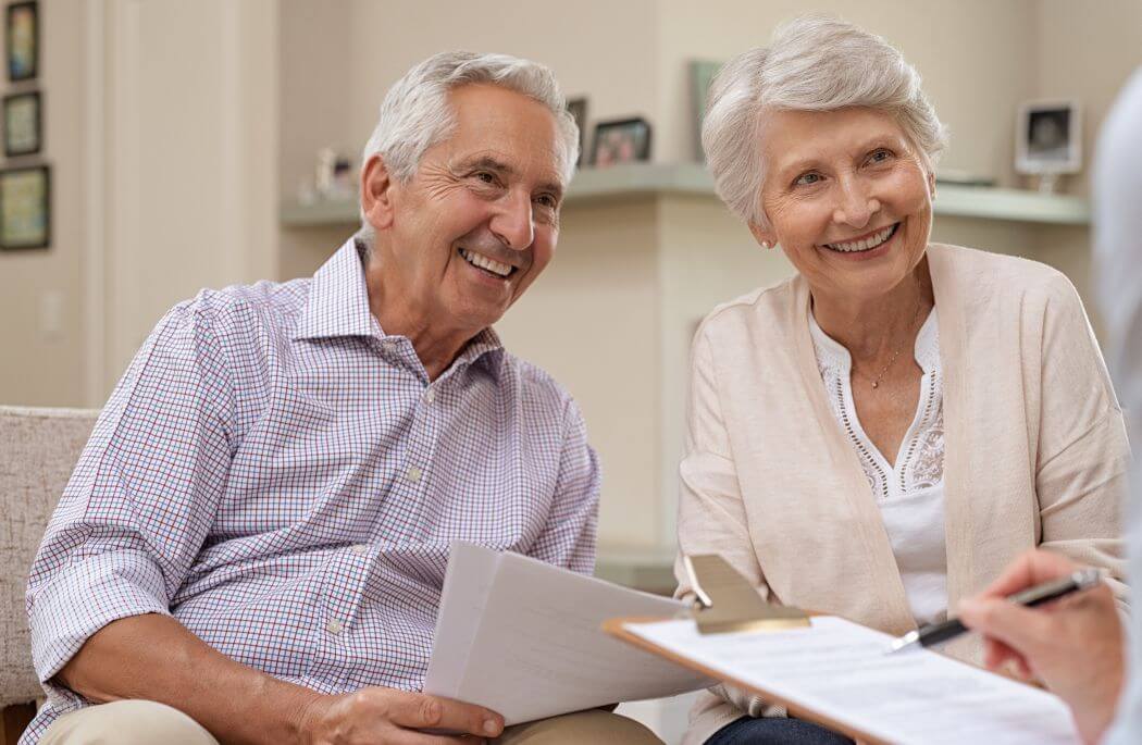 Couple smiling, holding advice documents and receiving cheering advice from their retirement planning financial adviser as they move toward a transitioning to retirement