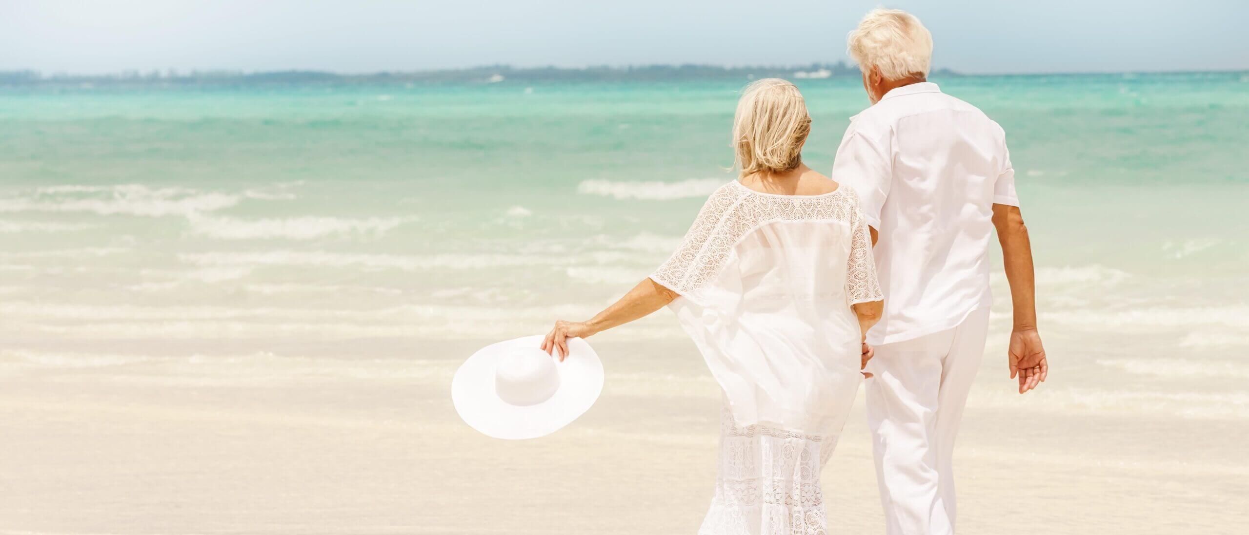 couple casually dressed, walking hand-in-hand along the sunlit beach with a calm sea beyond, relaxing in the knowledge that estate planning flexibility protects their estate