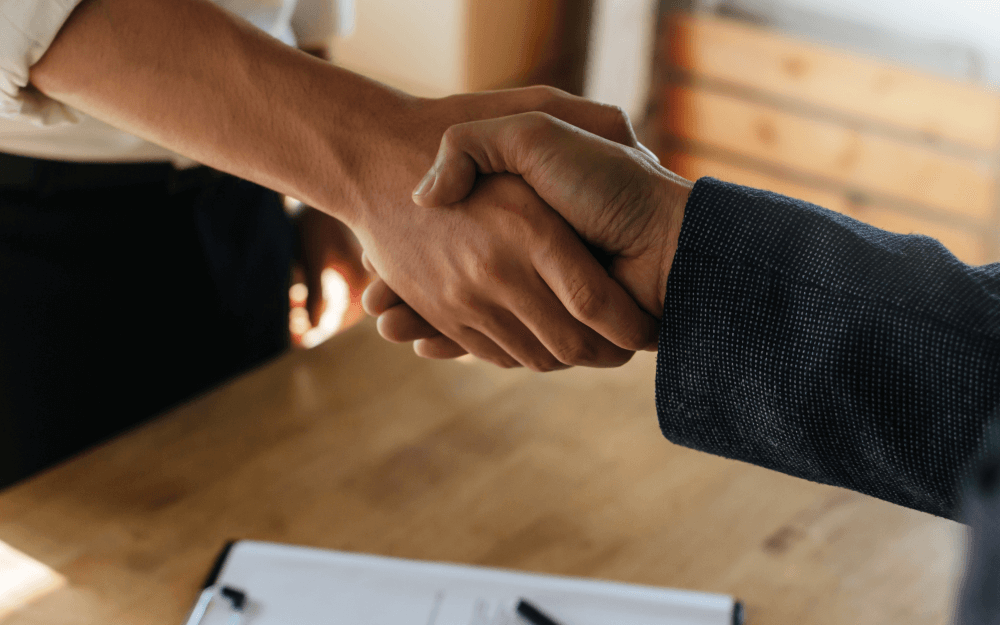 business people shaking hands across a desk after signing a business succession arrangement document