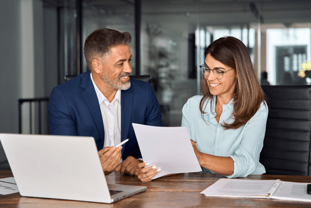 happy young female client reviewing risk profile printout with her young male financial planner, sitting at a desk in an office Risk profile for investor confidence