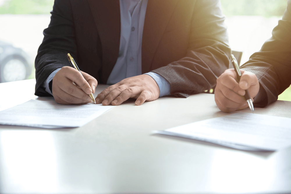 men at desk signing documentation for an assignment they have together - one seeking assistance with estate administration from the other