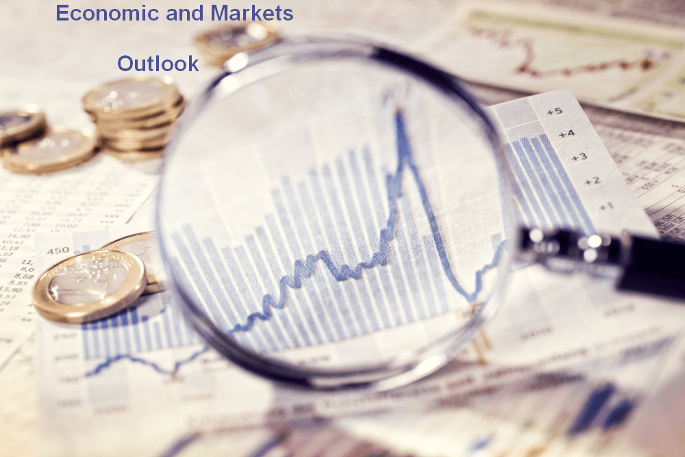 magnifying glass held over a table covered with charts and coins signifying an outlook on economic and market conditions