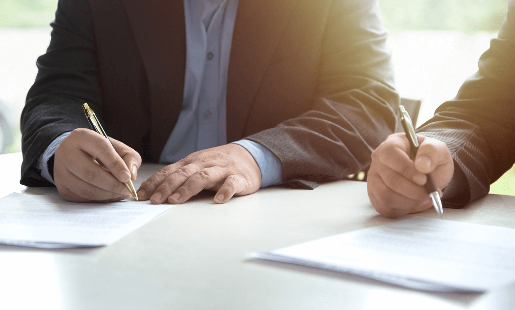 two business people sitting aside each other and signing contractual agreements for estate planning and business succession planning