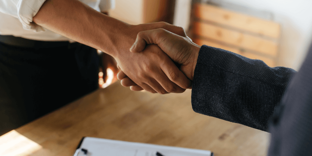 two males shake hands across a desk on which an agreement they have documented has been formalised - for us, a partnership-shareholder agreement