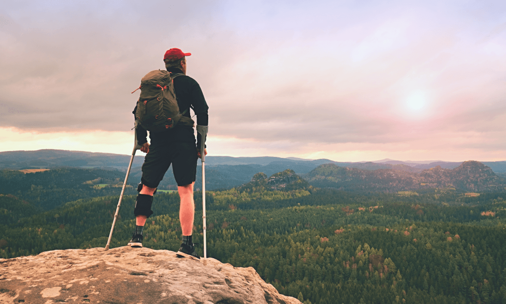 man on crutches standing atop a rock escarpment looking out into the extensive environment in front of him, reflecting on the value of trauma insurance to his wealth protection and health recovery