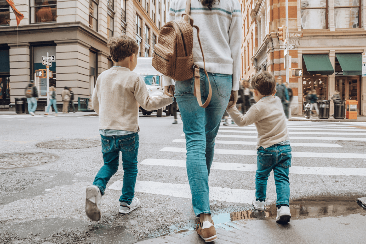 a mother leads her two young boys (all dressed similarly in denim pants and white pullovers) across a road - heading into the unknown, considering changed financial goals as life events occur