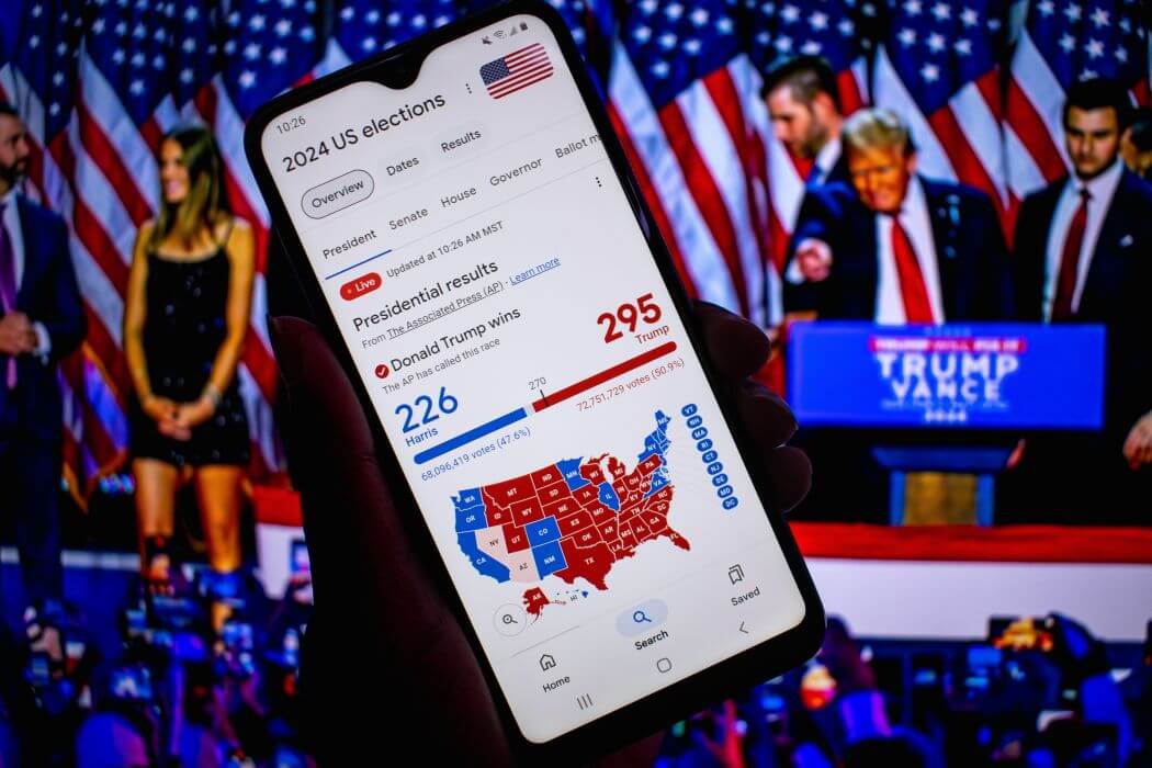 President-elect D J Trump at a celebration event of his 2024 election win, with a foreground of a smart phone with the screen showing the extent of his win - what are the consequences of the 2024 US election outcome?