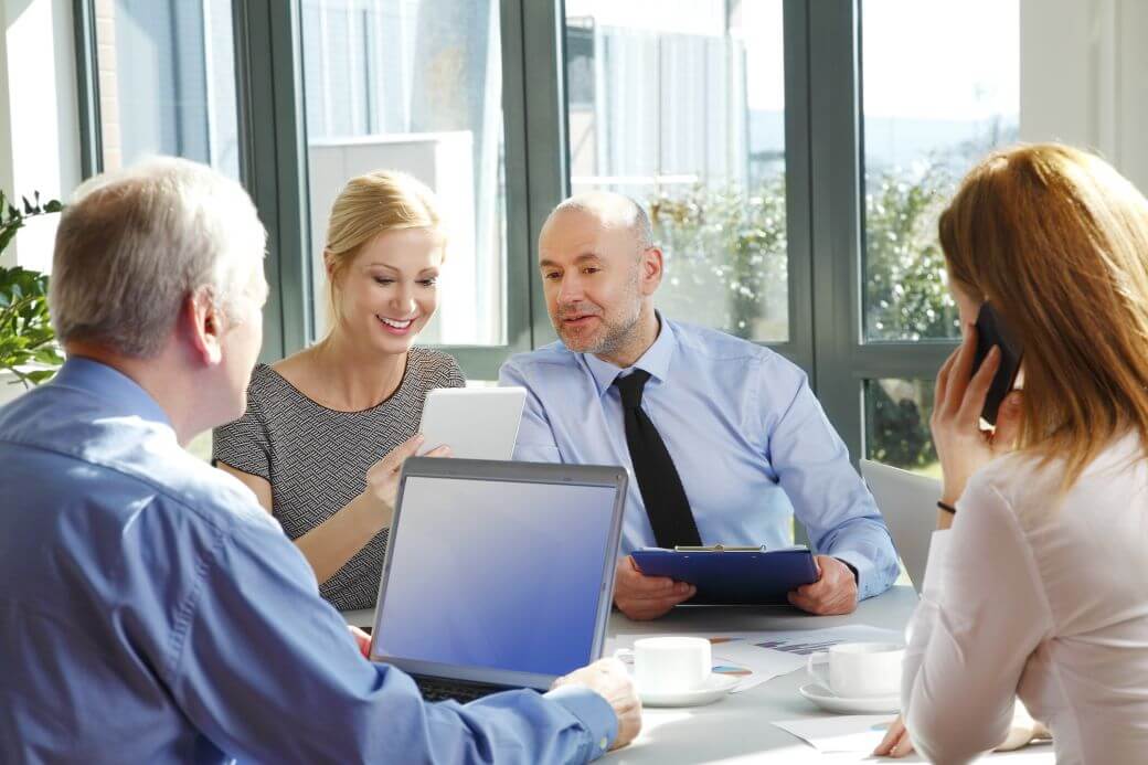 four trustees of an SMSF meeting around a table discussing papers and reports on devices to contemplate investment strategies and estate planning matters