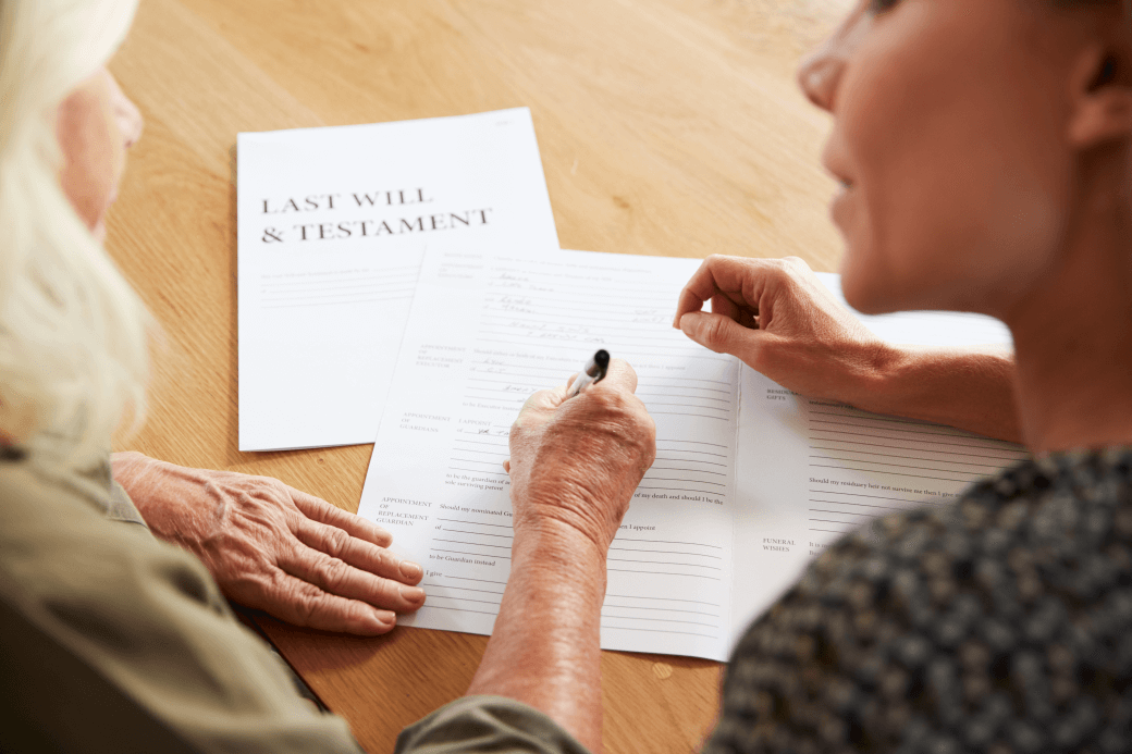 Aged woman completing a Will document in the presence of another, younger woman as part of her estate planning