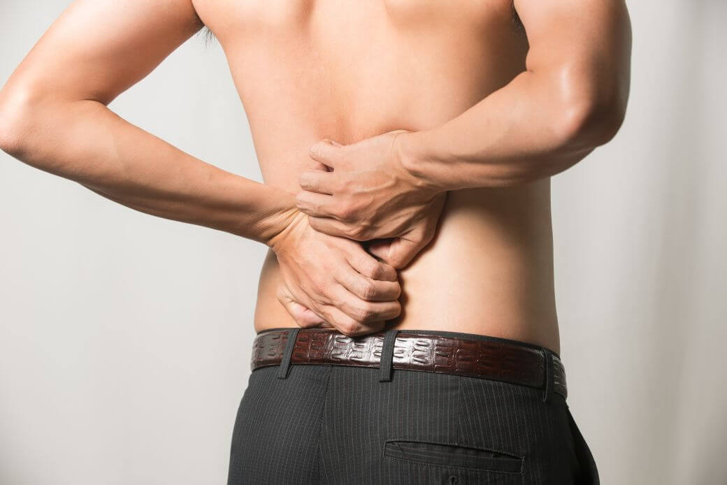 shirtless young man with back to camera as he clutches his back in pain