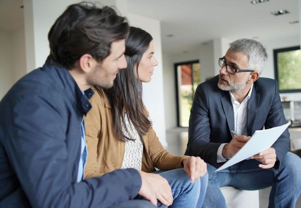 young couple discussing retirement planning strategies with financial planner in their home living room: the adviser is in blue jeans and a matching jacket; the couple are casually dressed