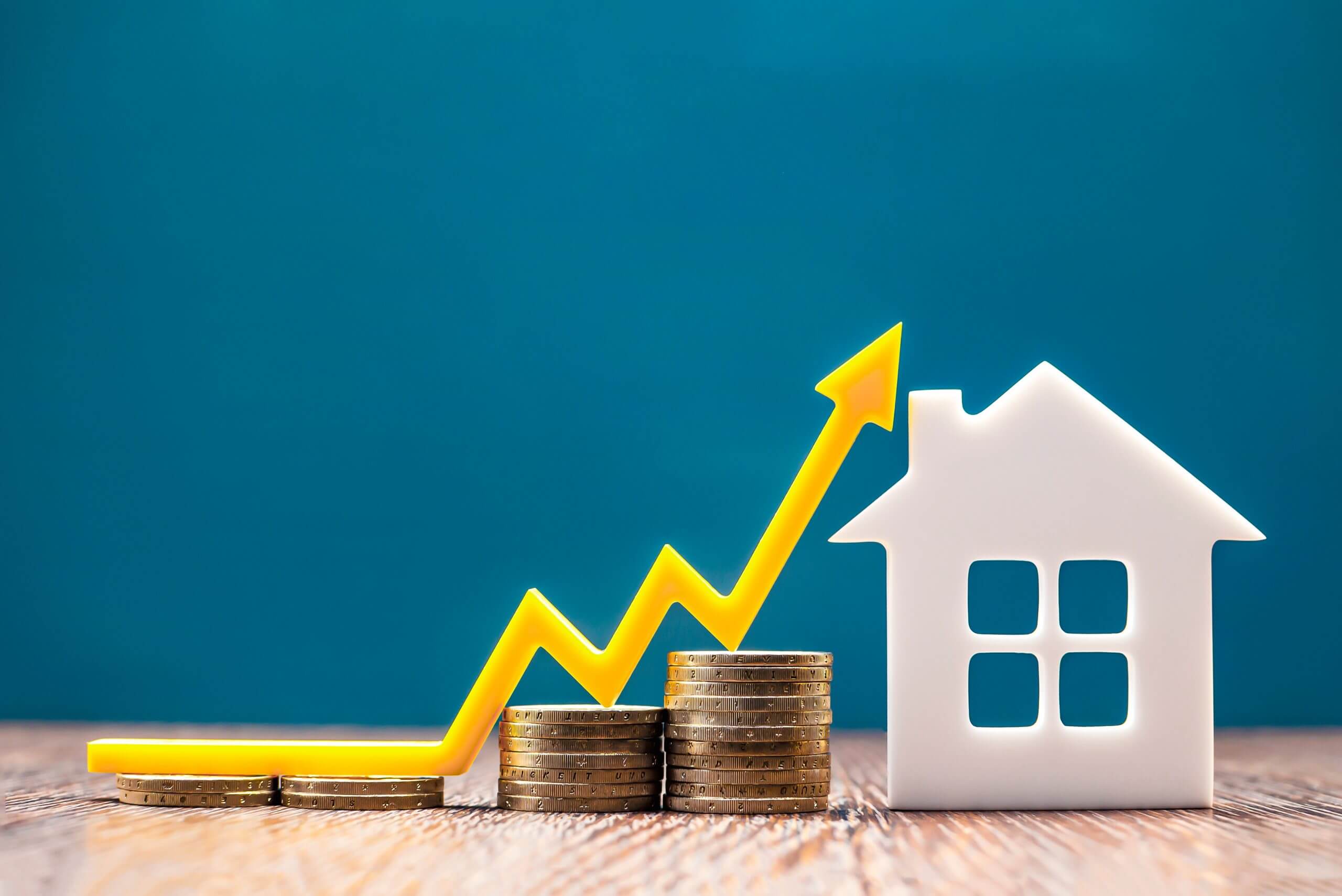 house model on a bench against a teal blue background and alongside coin stacks accumulating as they are closer to the house. there is a market index arrow, coloured yellow, indicating a volatile, but upward direction as debt recycling benefits the disciplined investor as they reduce the hpme mortgage and increase investments